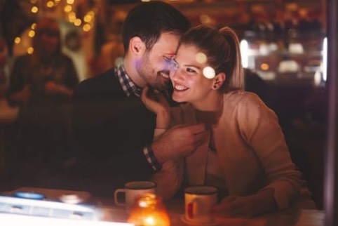 How much should I spend on dating?- a young couple on a date visibly in love, holding on to one another on a date in a pub