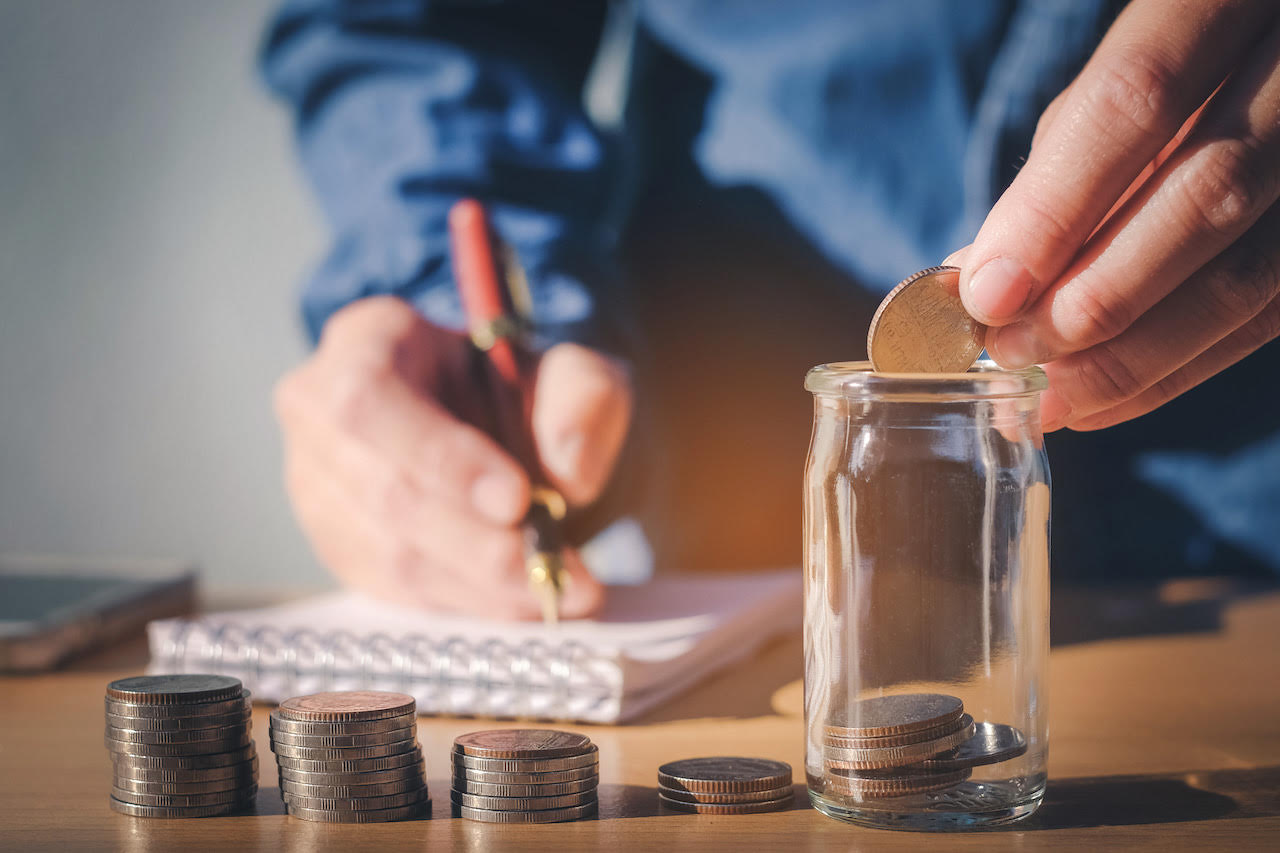 A man is putting money into a money jar, which is one of the best ways to save money