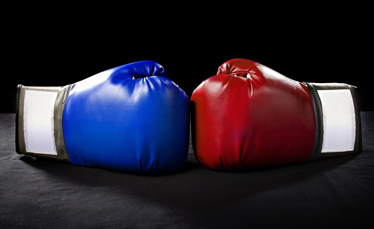 Defensive vs aggressive investor: Two boxing gloves, one blue (left) and one red (right) sit opposite one another, touching one another!