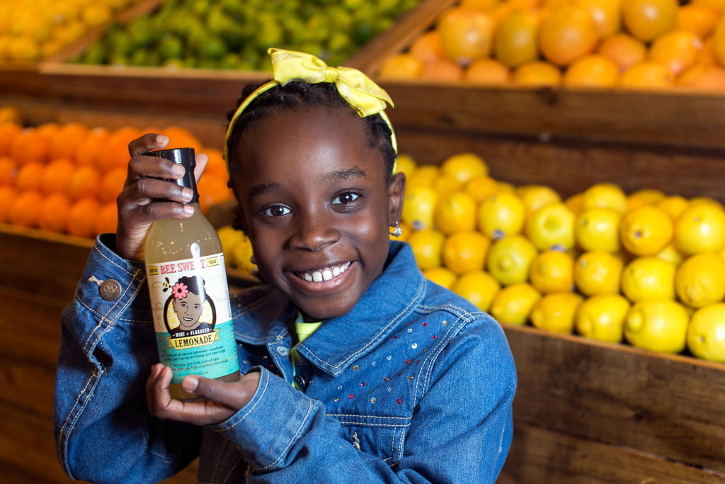 Mikaila Ulmer: a young woman holds up a bottle of lemonade in front of assorted fruits