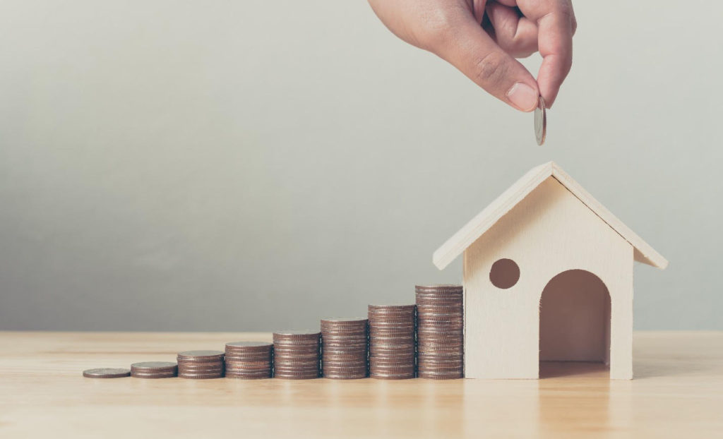 Types of investments: a hand placing coins down building up to a wooden house.