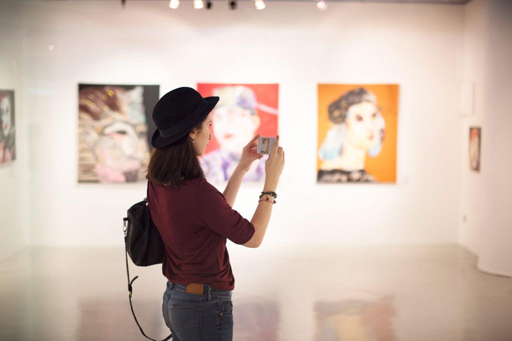 Invest in art: A young woman taking pictures of art on her phone in an art gallery
