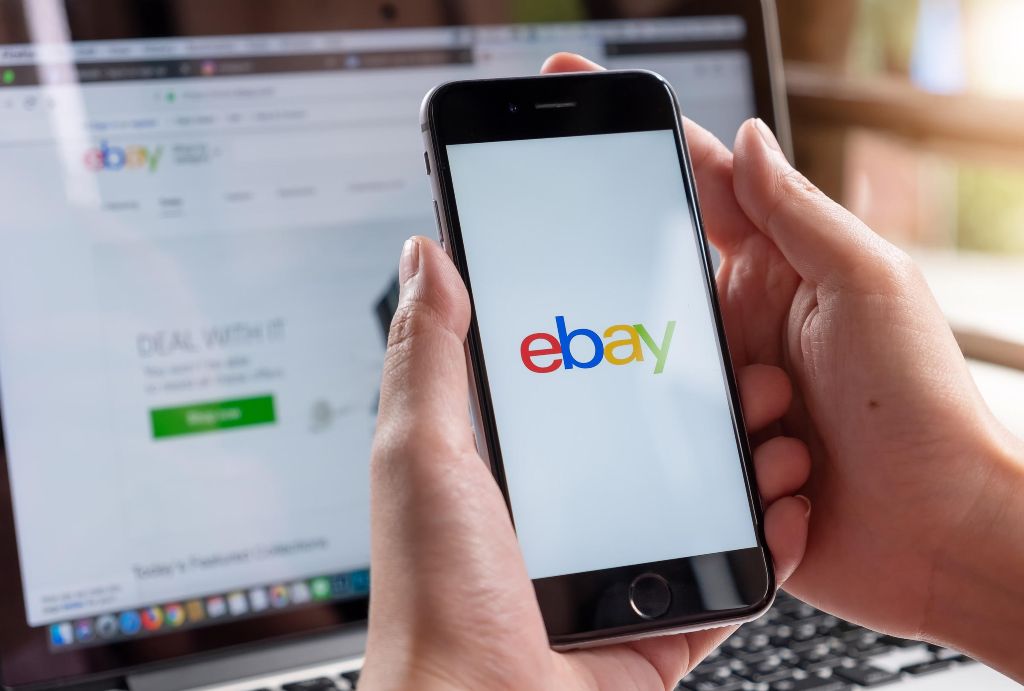 Most expensive things ever sold on eBay: a man logging in to eBay on his phone, with eBay open on his computer 